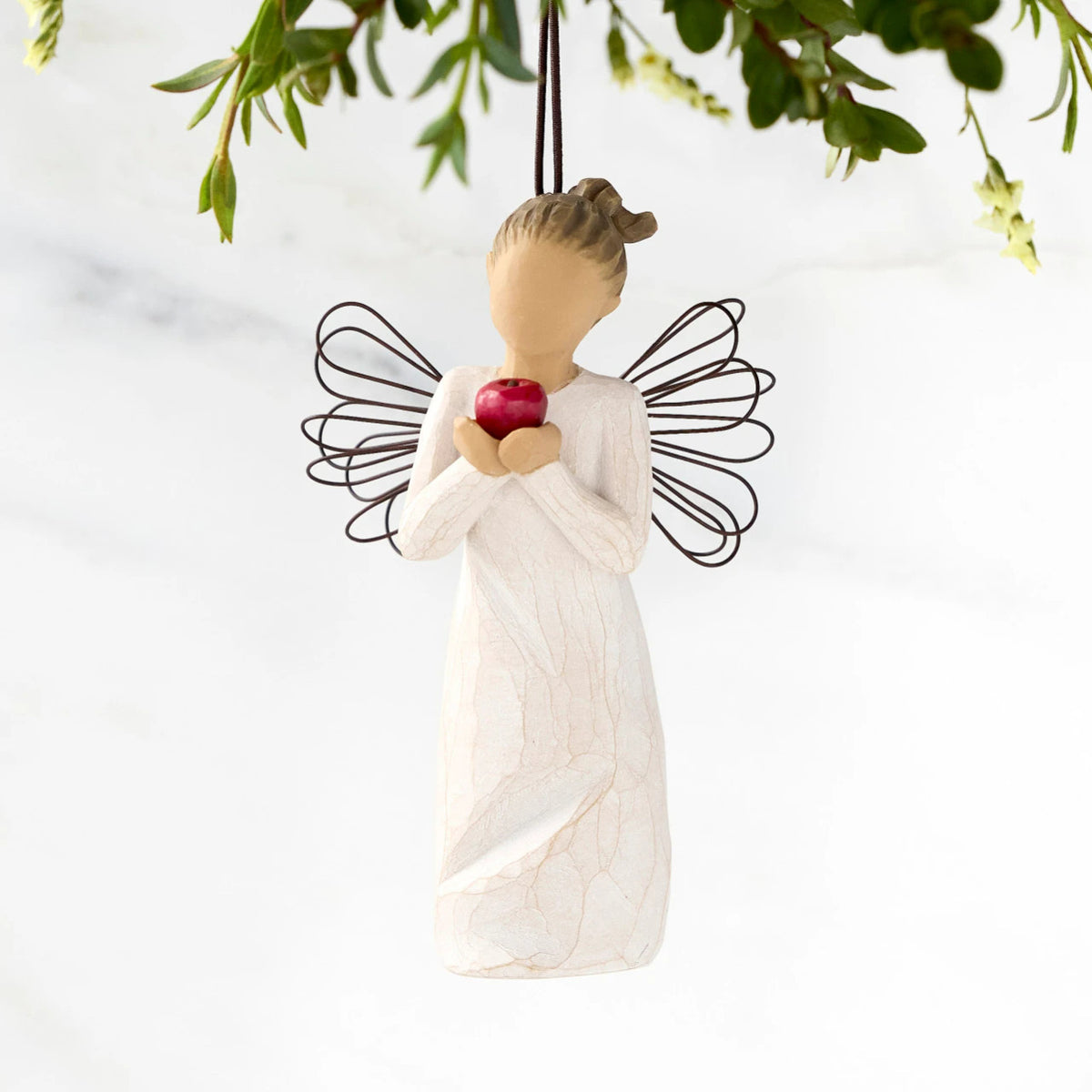 Front view of figure in cream dress with wire wings holding large red apple in hands, ornament hook on head