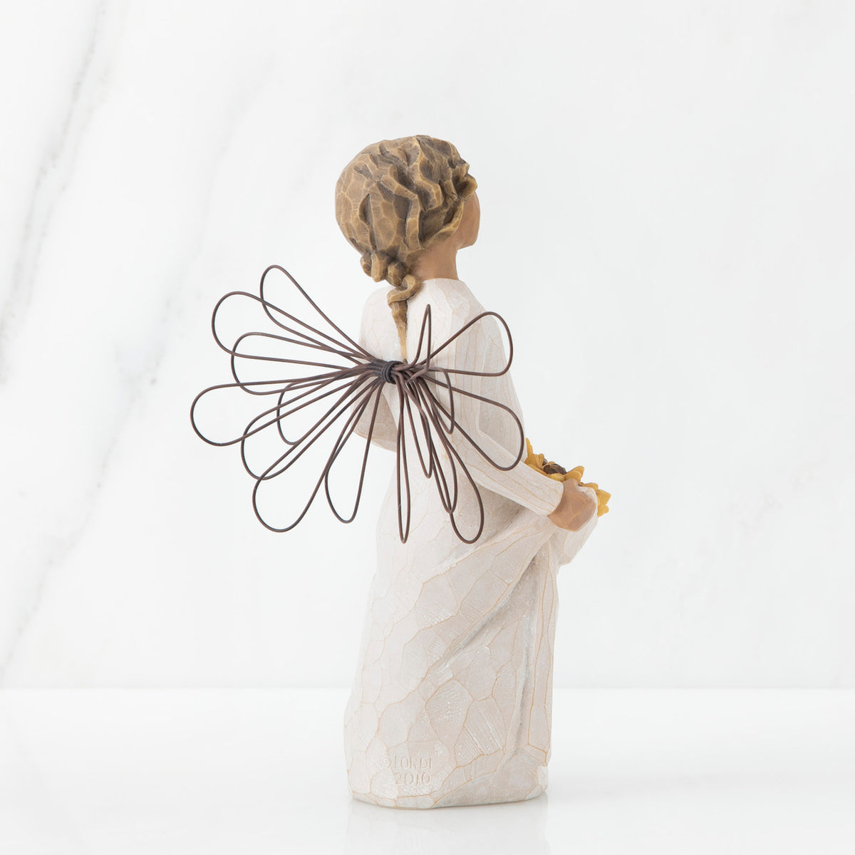 Back view of angel with tied back, curly, dark brown hair holding up a portion of her dress's skirt as it is full of sunflowers