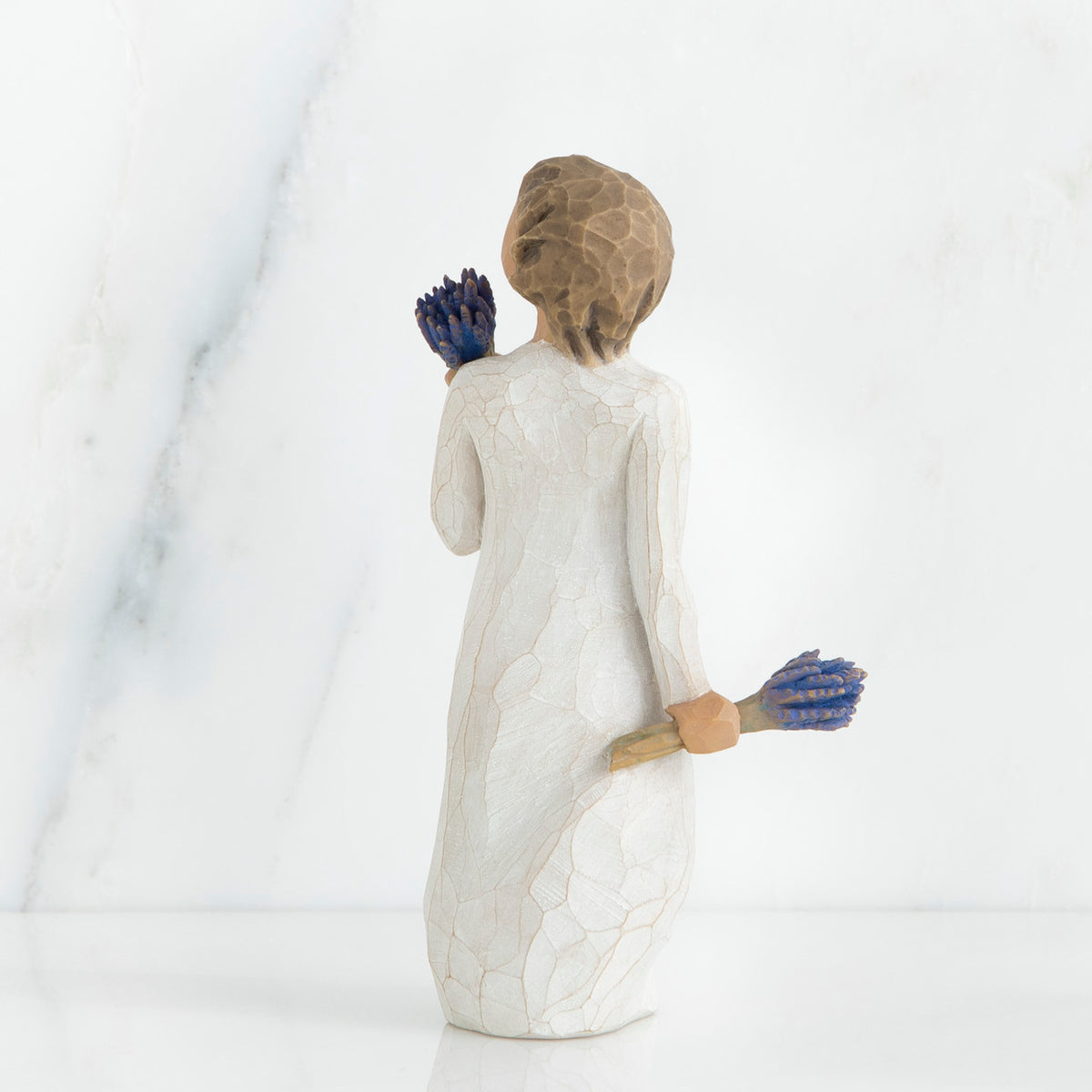 Back view of brunette girl figurine in white dress holding blue flowers