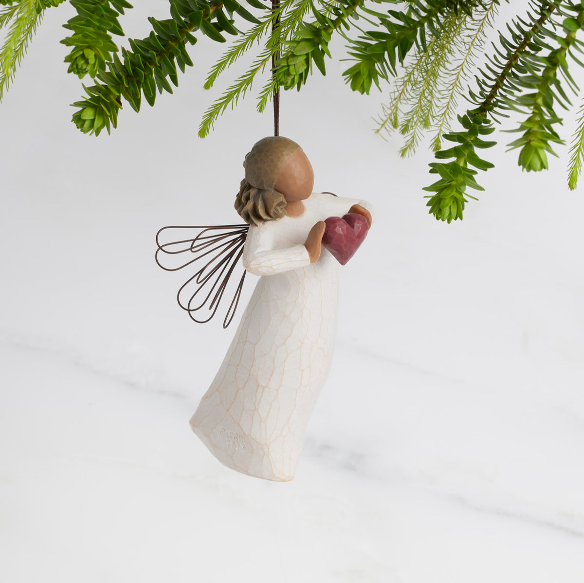 Facing right: Darker-skin Angel with wire wings holding red heart. Loop and hook attached in wings
