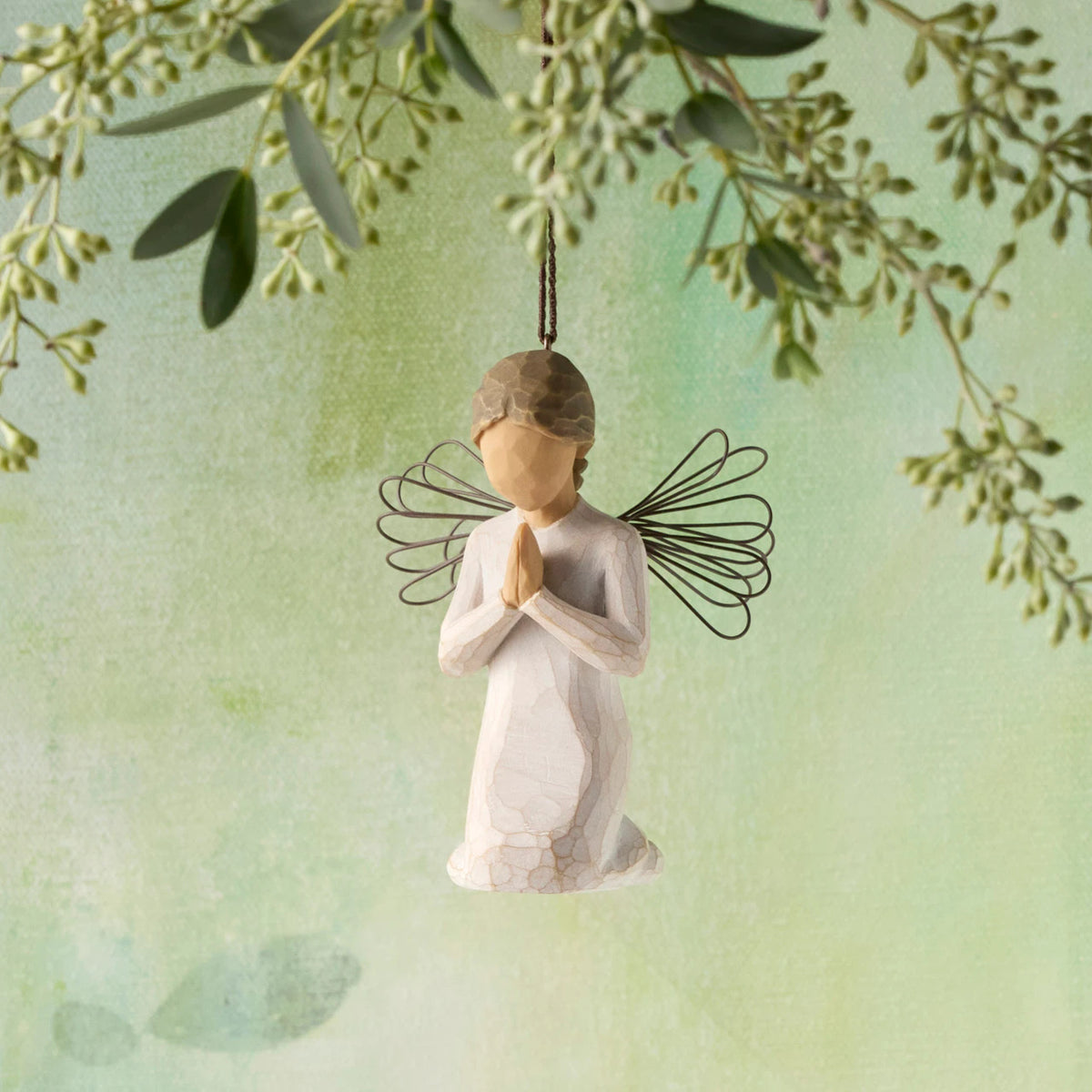 Willow Tree Angel of Prayer Ornament, 3"h hand-painted kneeling resin figure in cream dress with wire wings, hands in prayer position, brown elastic cord, hanging in front of green painting