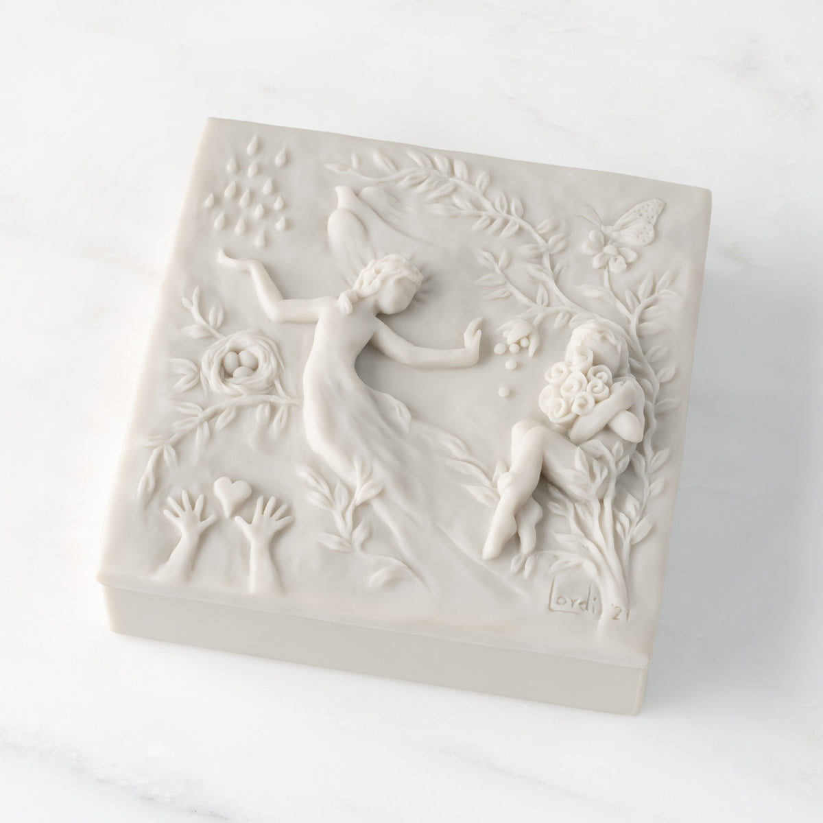 Closed white resin square box; lid carved with figural and organic imagery